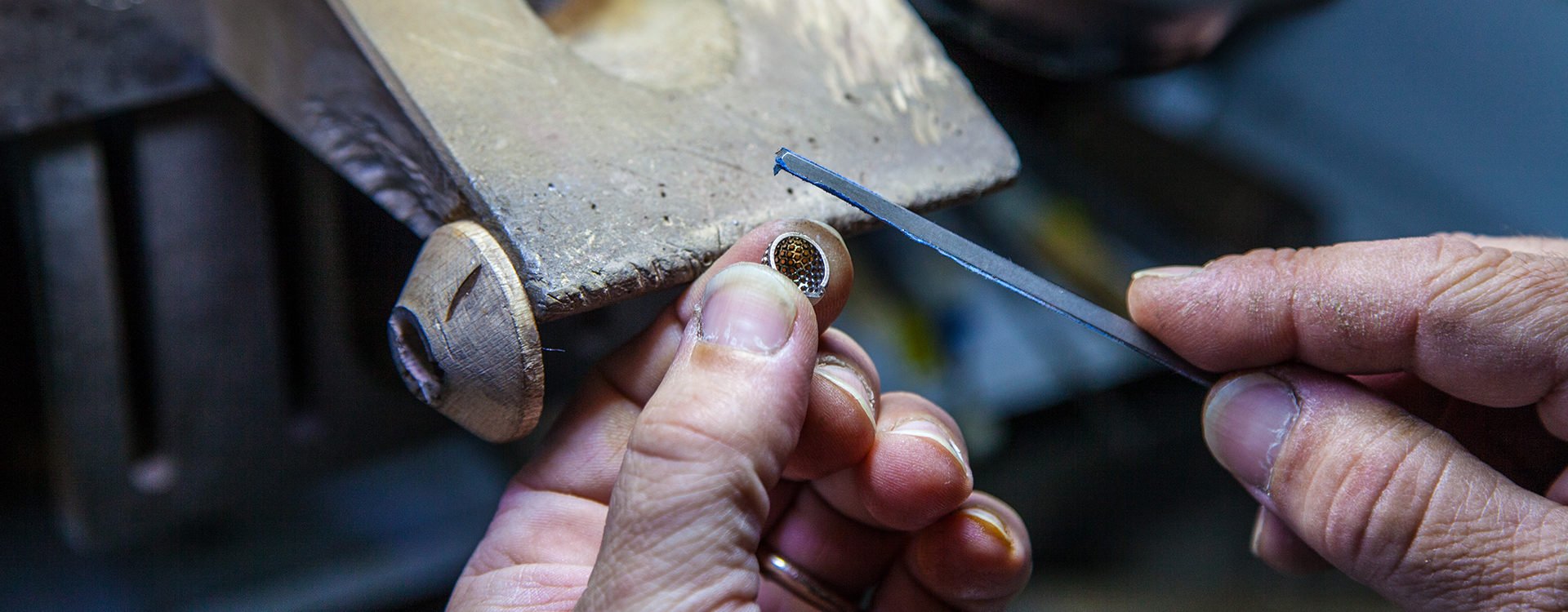 Mani di un orafo che rifiniscono un anello con la lima al banco del laboratorio